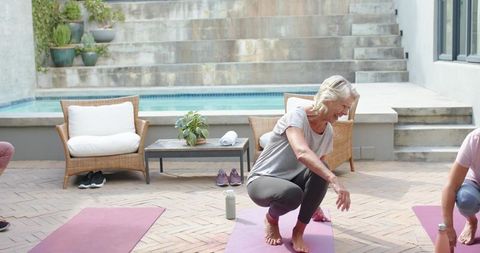 Senior woman practicing outdoor yoga on poolside patio with friends during morning wellness class