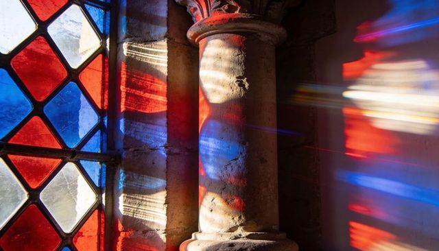 Bathing weathered column in red and blue stained glass light at historic chapel
