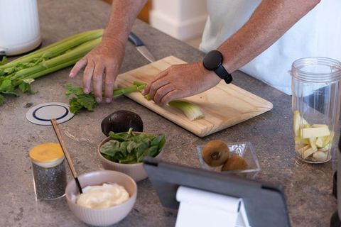 Mature man chopping celery for green smoothie meal prep with tablet and fresh produce