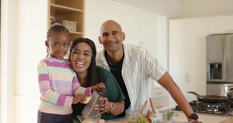 Multiracial family cooking together on bright kitchen island grating ingredients and smiling