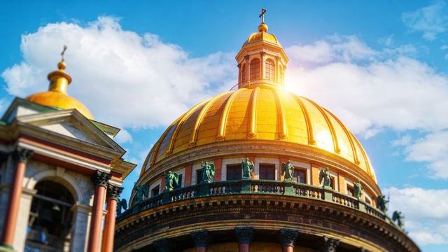 Gilded cathedral dome shining in sunlight with bronze statues and cupola