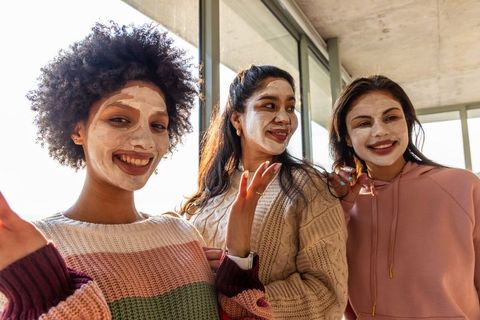 Diverse friends enjoying facial masks and cozy skincare night in sunlit modern apartment