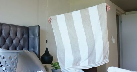 Holding striped towel covering face while lifting above bed headboard in contemporary bedroom