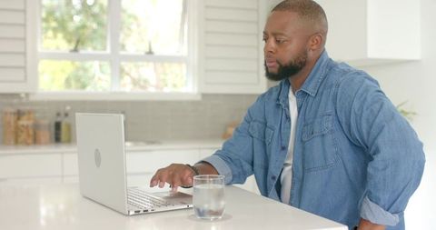 Man working on laptop at bright modern kitchen island for remote work and home office