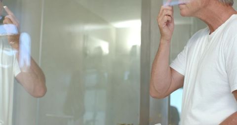 Mature man shaving at minimalist bathroom mirror reflecting calm morning grooming routine