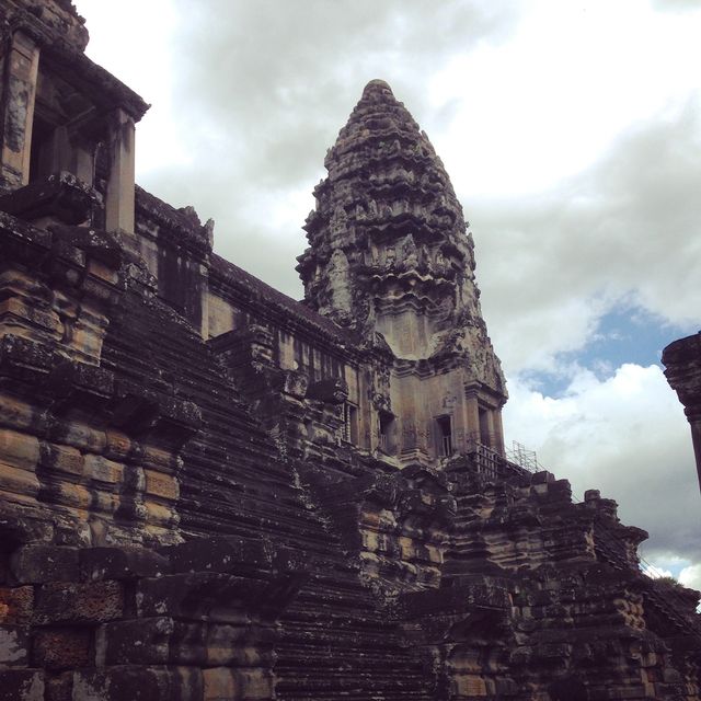 Image of Angkor Wat temple showcasing its ancient stone architecture under a cloudy sky. Perfect for use in travel blogs, cultural heritage articles, archaeological publications, and promotional material for tourism in Cambodia.