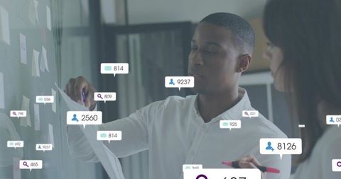 Collaborating team at glass wall with analytics and sticky notes for data-driven planning