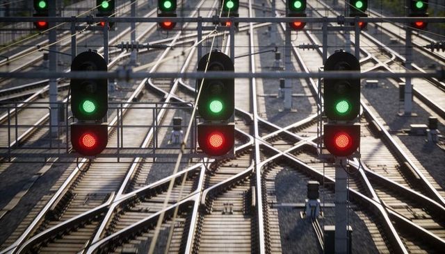 Glinting signal gantries with red and green lights above railway junction in sunlight