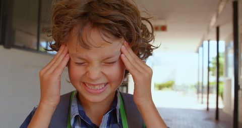Frustrated schoolboy rubbing temples in corridor