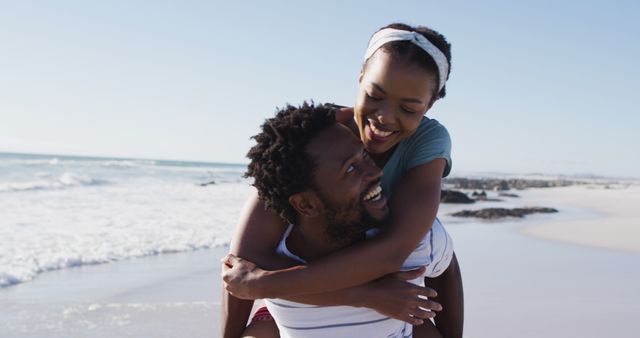 African american man carrying african american woman piggyback on the beach. healthy outdoor leisure time by the sea.