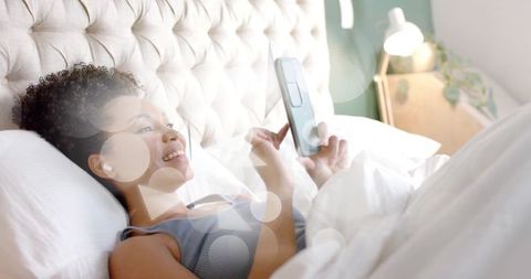 Woman Relaxing in Bed Using Smartphone with Digital Interfaces