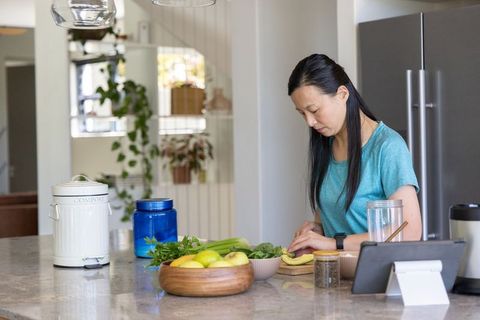 Mature asian woman preparing healthy breakfast kitchen island slicing banana with compost