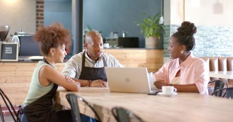 African american cafe team collaborating on menu and service using laptop in coffeeshop