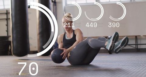 Woman athlete performing medicine ball russian twist on gym floor with fitness hud overlays