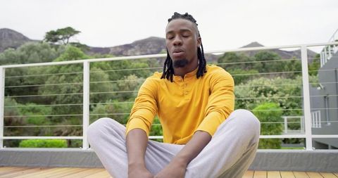 African American man meditating on balcony in mustard henley and loungewear