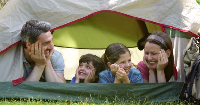 Family of four bonding and smiling inside camping tent on sunny day. Perfect for advertising family trips, outdoor activities, camping gear, and leisure time in nature.