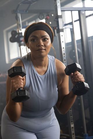 African american woman lifting dumbbells in gym, focused strength training in light blue activewear
