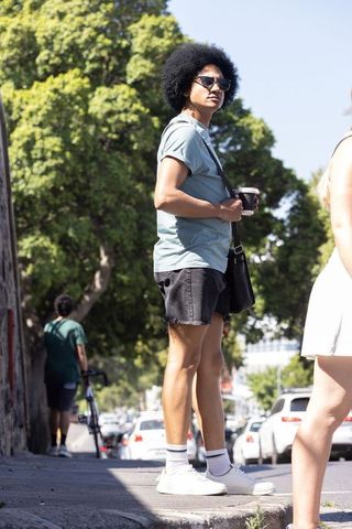 African american man standing on curb holding coffee wearing sunglasses and crossbody bag