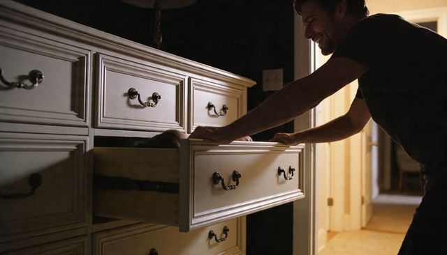 Laughing father leaning over dresser while child peeking from drawer in cozy warm home