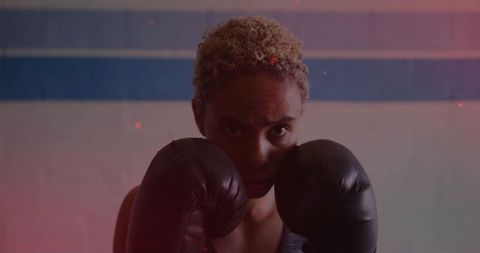 Female boxer raising gloves in moody gym portrait intense focus strength training