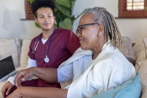 Senior african american woman receiving compassionate home healthcare visit from nurse