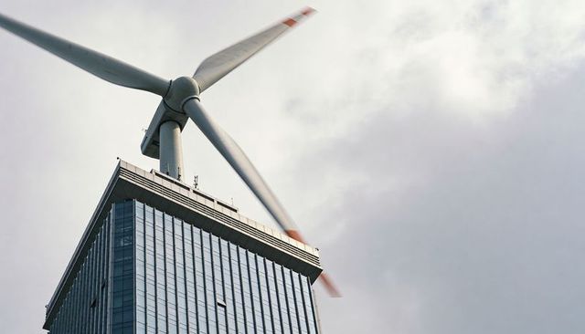 Rotating wind turbine atop glass skyscraper rooftop with red-tipped blades
