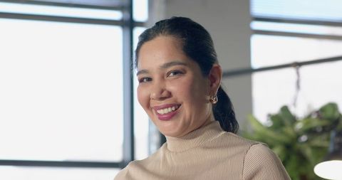 Confident professional woman smiling at window in modern office headshot natural light