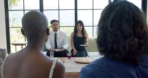 Dressed friends sharing dessert and drinks in modern living room with large windows