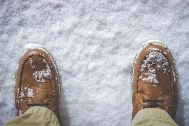 Person is standing outside in snow wearing brown leather shoes, giving the appearance of a casual winter day. This image can be used for themes related to winter fashion, outdoor activities, cold weather, or seasonal changes.