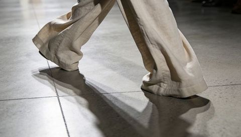 Walking wide-leg linen trousers rippling on polished tile with dramatic shadow