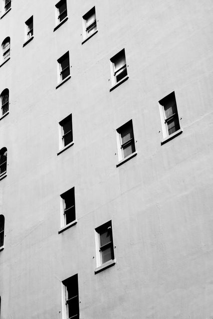 Black and white close-up of a classic urban building exterior featuring symmetrical windows. Ideal for use in marketing materials, architectural portfolios, design studies, or cityscape presentations. Suitable for projects emphasizing urban life, minimalism, or classic architectural styles.