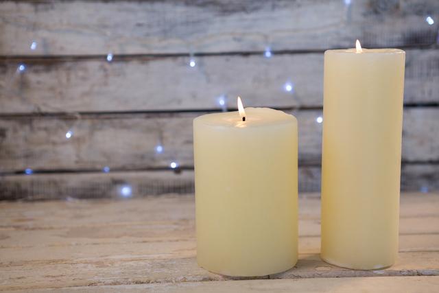 Two candles are burning on a rustic wooden plank with soft Christmas lights in the background. This image evokes a warm and cozy holiday atmosphere, perfect for use in Christmas cards, holiday advertisements, or seasonal blog posts.