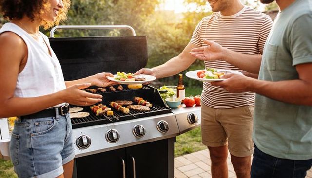 Friends grilling on stainless steel gas grill at backyard cookout serving skewers and burgers