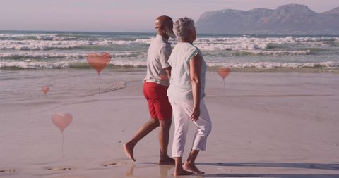 Senior Couple Walking on Sunny Beach with Heart Balloons
