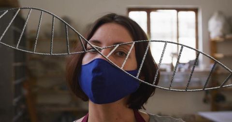 Artist inspecting wire helix sculpture while wearing protective mask in sunlit studio