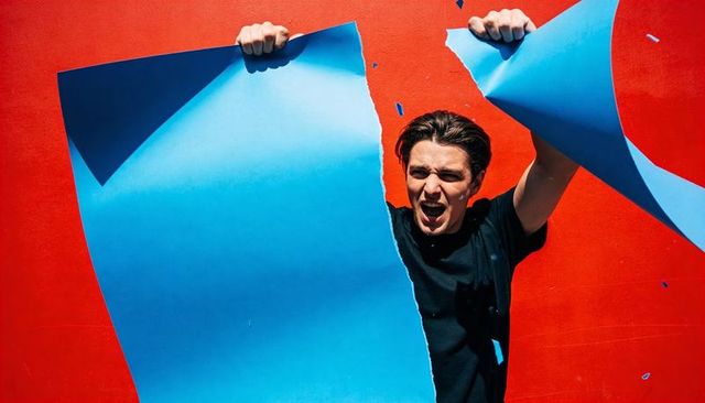 Young man tearing bright blue poster from red wall for dynamic ripped-paper reveal