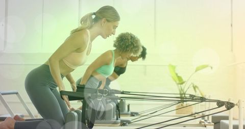 Women training on pilates reformers pulling resistance straps in sunlit studio group class