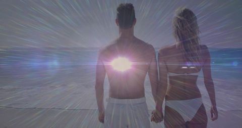 Backlit couple walking hand in hand on beach with radiant sunburst lens flare