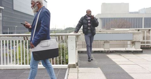 Mature african american professionals walking and checking smartphones on urban bridge