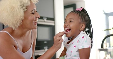 Joyful Mother Feeding Daughter in Bright Kitchen Moment