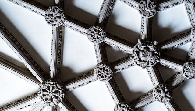 Intricate gothic ribbed vault ceiling with carved bosses and floral rosette geometry, historic chape