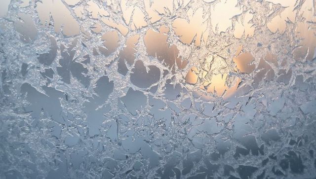 Crystal frost lace on window glass with warm sunrise backlight, frozen texture backdrop