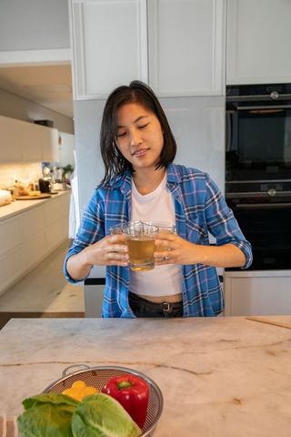 Woman Holding Beverages in Modern Kitchen with Fresh Vegetables