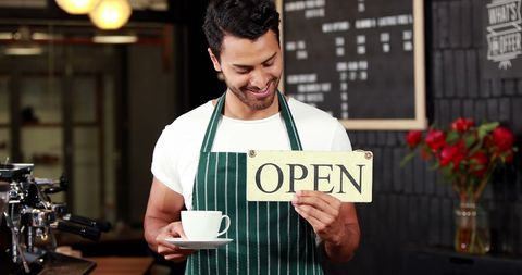 Smiling Young Barista Holding Open Sign in Cafe