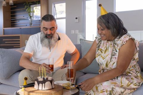 Mature couple celebrating birthday at home cutting cake and toasting with champagne