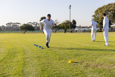 Cricket players sprinting through cone drill on sunny grass training field building agility and spee