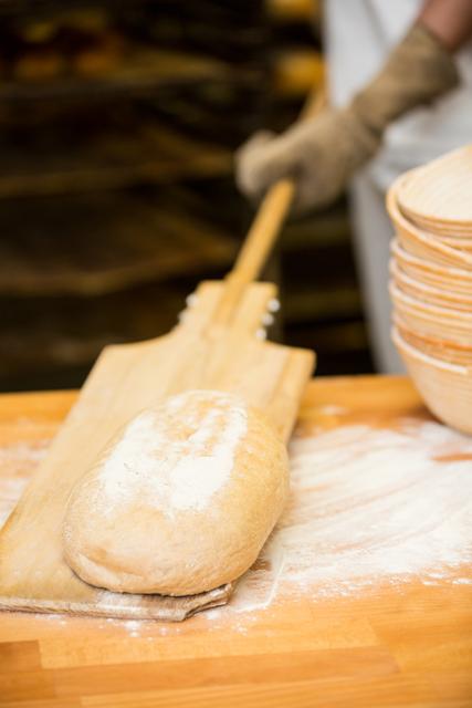Baker lifting bread dough in wooden spoon for baking 