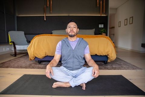 Mature asian man meditating on yoga mat in cozy bedroom during home mindfulness practice