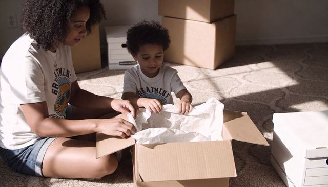 Mother and son unpacking boxes during move in sunlit home, family bonding moment