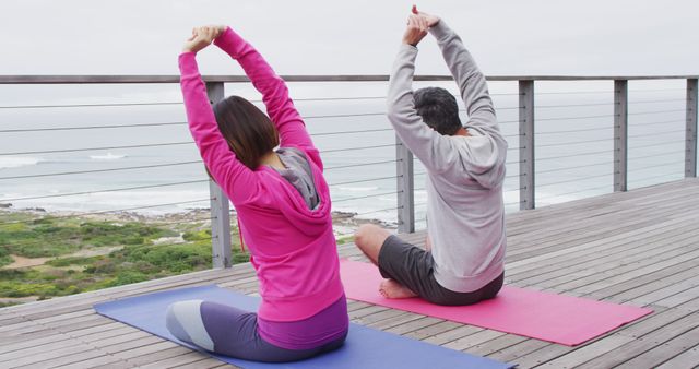 Happy diverse couple doing yoga, sitting and stretching on balcony. Spending quality time at home.